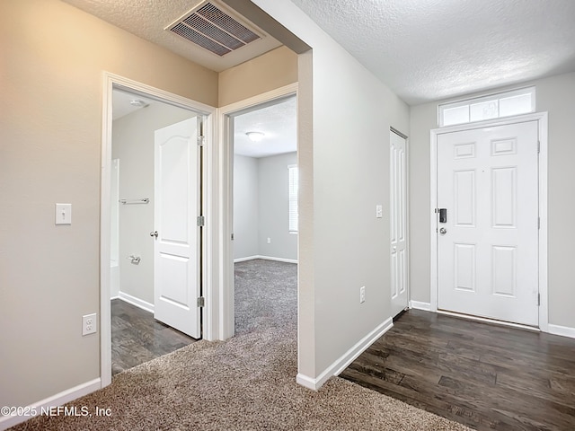 foyer entrance with a textured ceiling and dark colored carpet