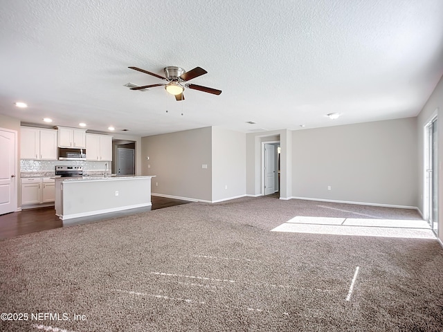 unfurnished living room with sink, a textured ceiling, ceiling fan, and dark colored carpet