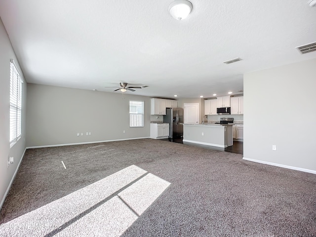 unfurnished living room with sink, ceiling fan, a healthy amount of sunlight, and dark colored carpet