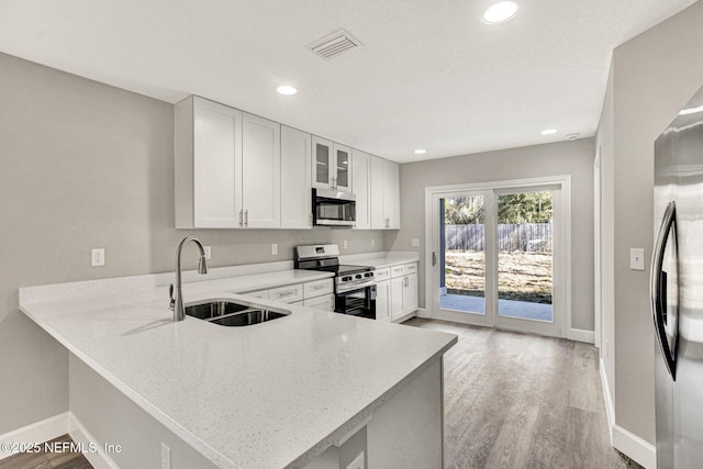 kitchen with stainless steel appliances, white cabinetry, light stone counters, and kitchen peninsula