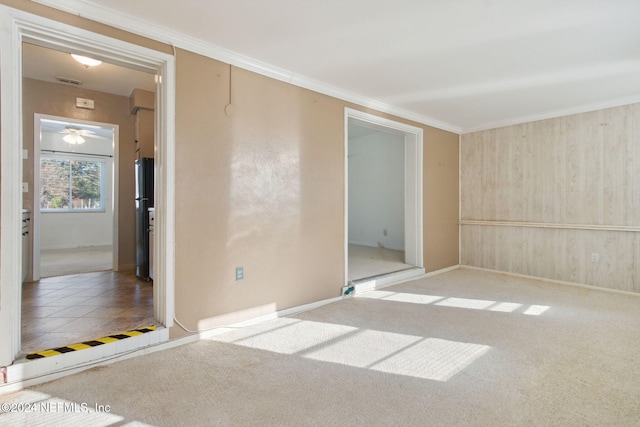 carpeted empty room featuring wooden walls, ceiling fan, and crown molding