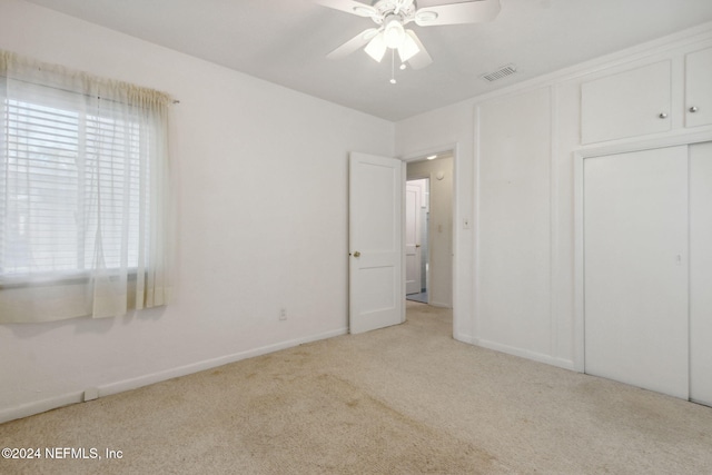 unfurnished bedroom featuring a closet, light colored carpet, and ceiling fan