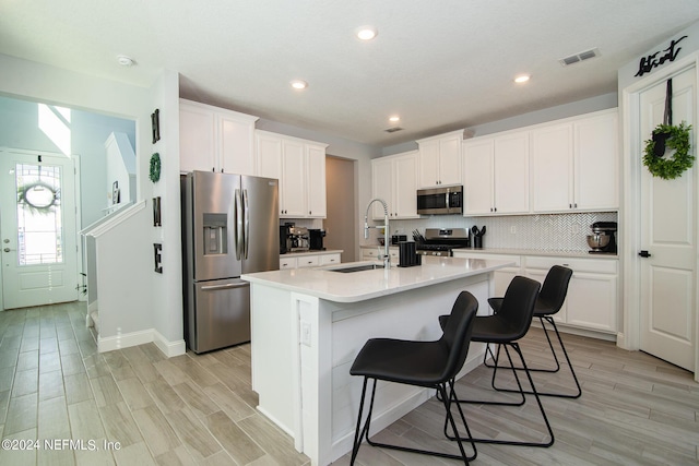 kitchen with appliances with stainless steel finishes, sink, white cabinetry, a breakfast bar area, and an island with sink