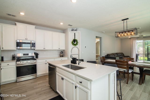 kitchen with white cabinets, sink, stainless steel appliances, and a kitchen island with sink