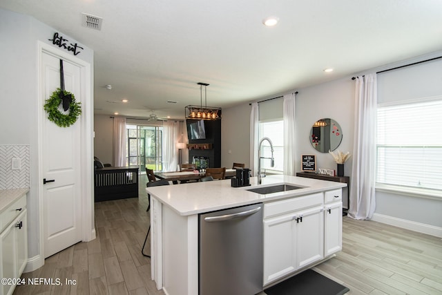 kitchen featuring a kitchen island with sink, sink, stainless steel dishwasher, light wood-type flooring, and white cabinetry