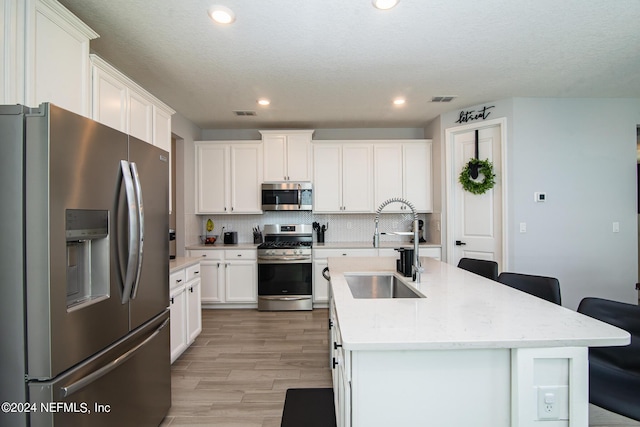 kitchen with sink, an island with sink, stainless steel appliances, and light hardwood / wood-style flooring