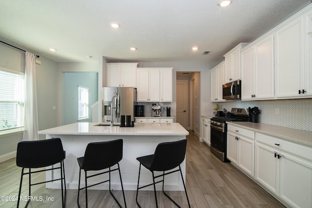 kitchen with white cabinetry, stainless steel appliances, tasteful backsplash, light hardwood / wood-style floors, and a center island with sink