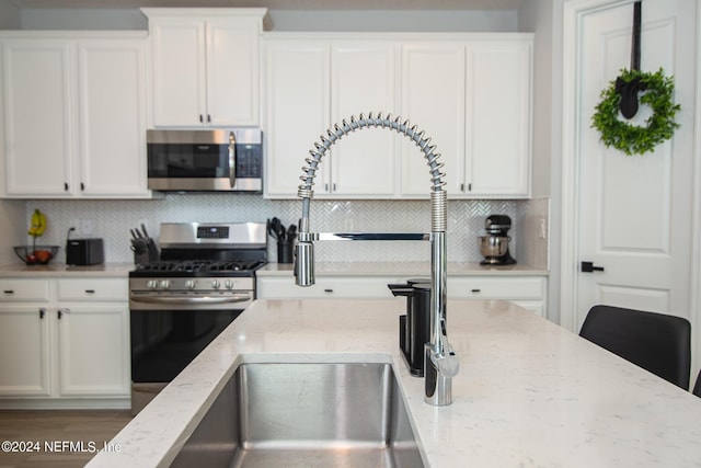 kitchen featuring white cabinets, appliances with stainless steel finishes, tasteful backsplash, and light stone counters