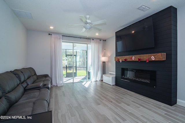 living room with ceiling fan, a fireplace, a textured ceiling, and light hardwood / wood-style flooring