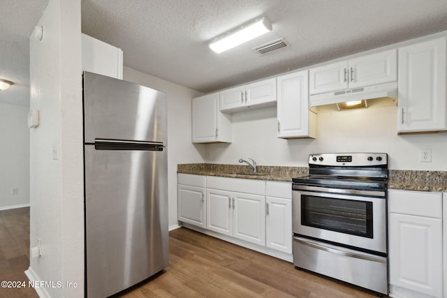 kitchen featuring a textured ceiling, dark stone countertops, light hardwood / wood-style flooring, appliances with stainless steel finishes, and white cabinets