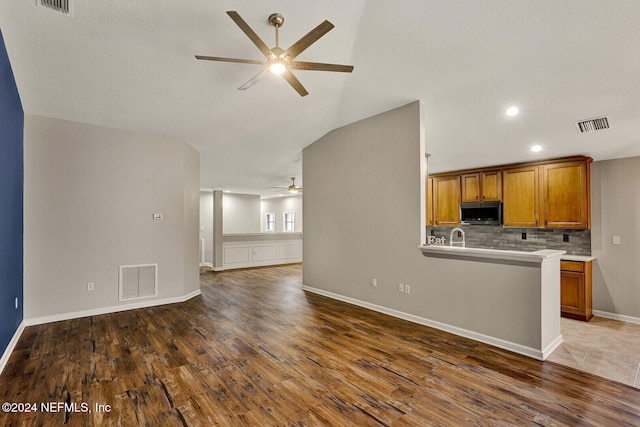 kitchen featuring kitchen peninsula, tasteful backsplash, ceiling fan, dark wood-type flooring, and lofted ceiling