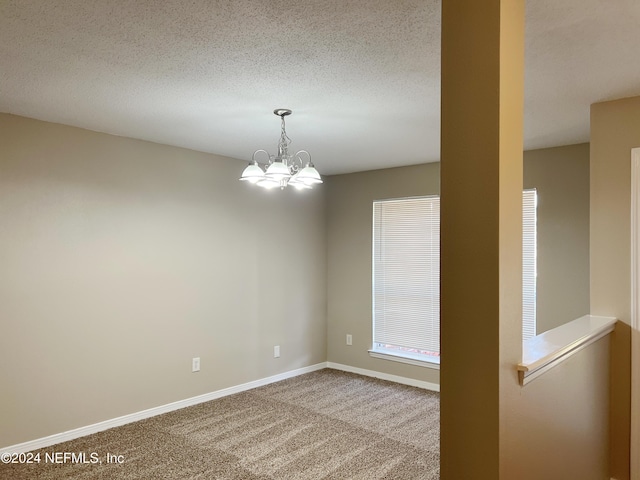 carpeted spare room featuring a textured ceiling and a notable chandelier