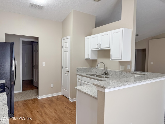 kitchen featuring kitchen peninsula, black refrigerator, light stone counters, sink, and white cabinets