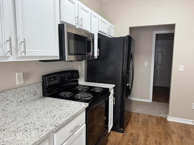 kitchen featuring white cabinets, black electric range oven, light stone counters, and light wood-type flooring