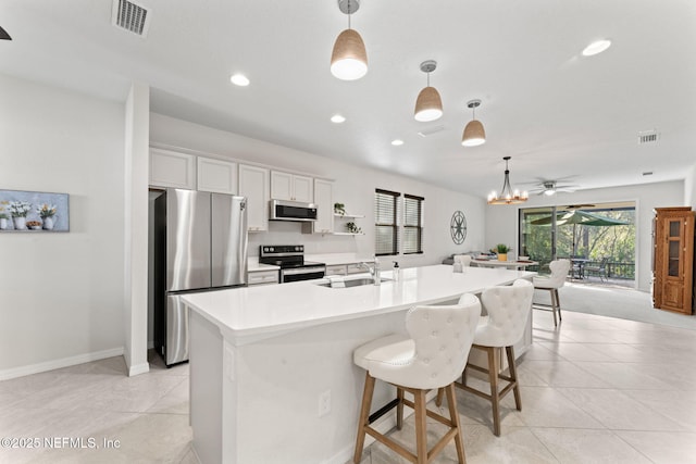 kitchen with stainless steel appliances, sink, decorative light fixtures, white cabinets, and an island with sink