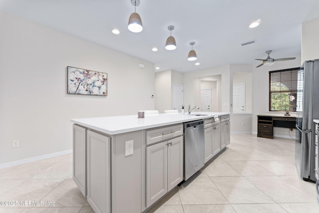 kitchen with appliances with stainless steel finishes, gray cabinetry, ceiling fan, decorative light fixtures, and a center island with sink