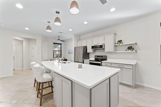 kitchen featuring appliances with stainless steel finishes, ceiling fan, decorative light fixtures, a center island with sink, and light tile patterned flooring