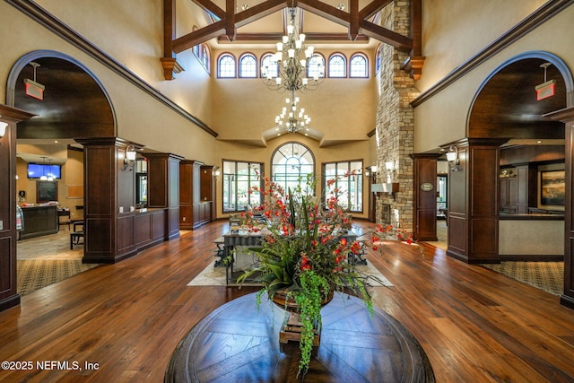 dining space featuring a notable chandelier, wood-type flooring, a towering ceiling, and ornate columns