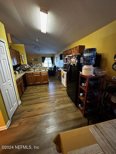 kitchen with black refrigerator, kitchen peninsula, a textured ceiling, dark wood-type flooring, and lofted ceiling