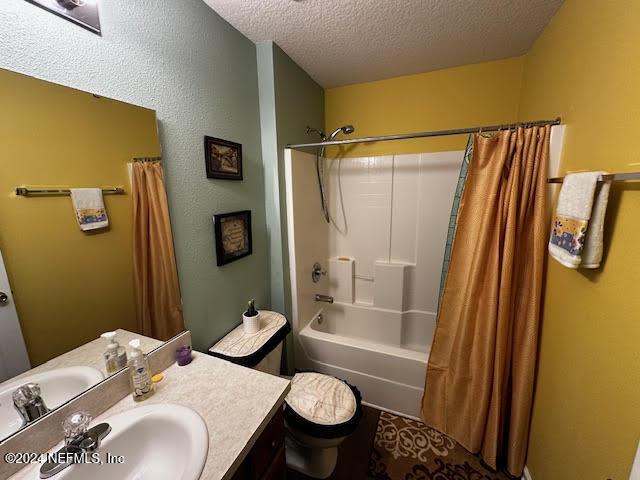 full bathroom featuring vanity, toilet, a textured ceiling, and shower / tub combo with curtain