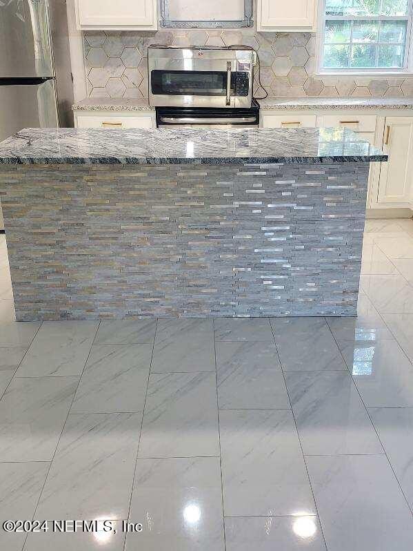 kitchen with light stone counters, white cabinetry, and backsplash