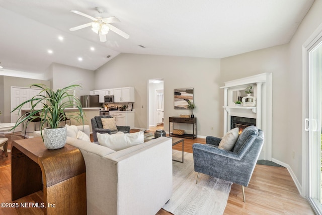 living room featuring ceiling fan, light hardwood / wood-style floors, and vaulted ceiling