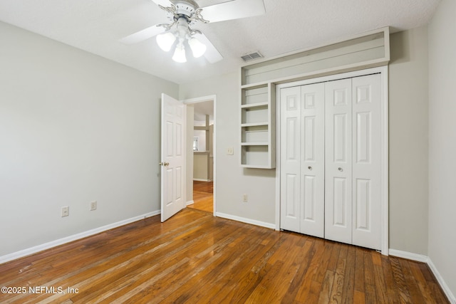 unfurnished bedroom with a textured ceiling, a closet, hardwood / wood-style flooring, and ceiling fan