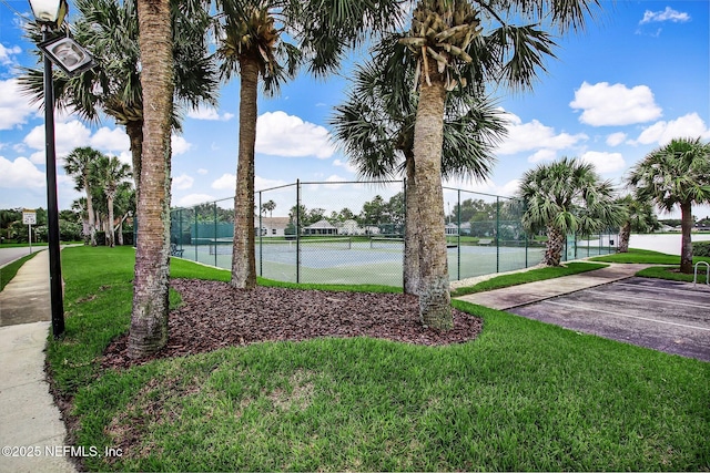 view of tennis court with a water view and a yard