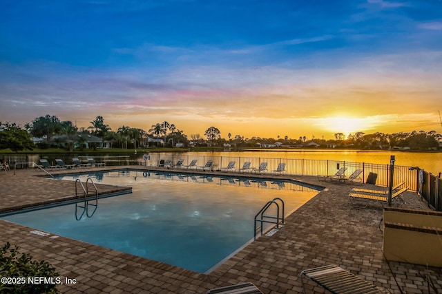 pool at dusk featuring a water view and a patio