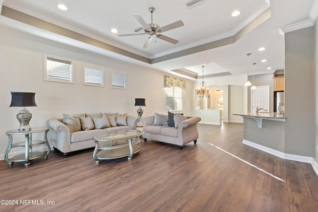 living room featuring a raised ceiling, crown molding, dark wood-type flooring, and ceiling fan with notable chandelier