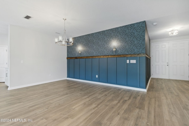 empty room with wood-type flooring and a notable chandelier