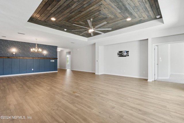 unfurnished living room with a tray ceiling, light hardwood / wood-style floors, and ceiling fan with notable chandelier