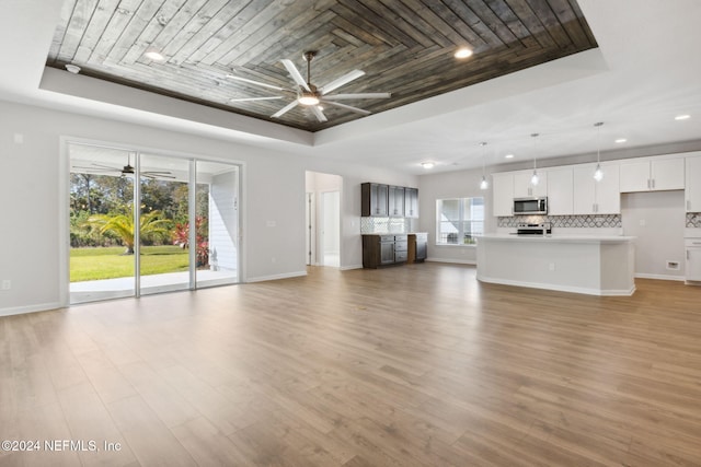 unfurnished living room featuring a tray ceiling, ceiling fan, and light wood-type flooring