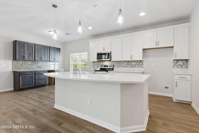 kitchen featuring hardwood / wood-style flooring, an island with sink, appliances with stainless steel finishes, decorative light fixtures, and white cabinetry