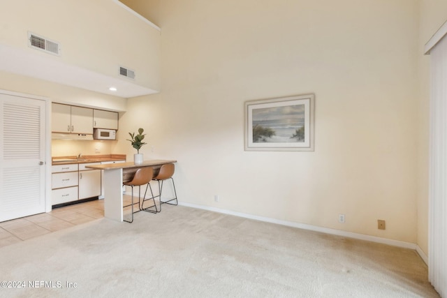 kitchen featuring light carpet, a high ceiling, cream cabinets, a kitchen bar, and kitchen peninsula