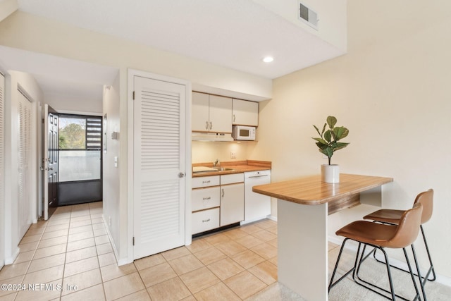 kitchen featuring white cabinets, white appliances, a breakfast bar area, and light tile patterned floors