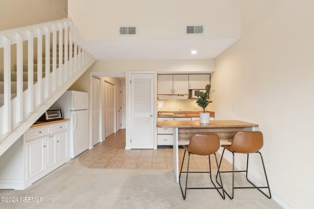 kitchen featuring a kitchen breakfast bar, light colored carpet, sink, white refrigerator, and butcher block counters