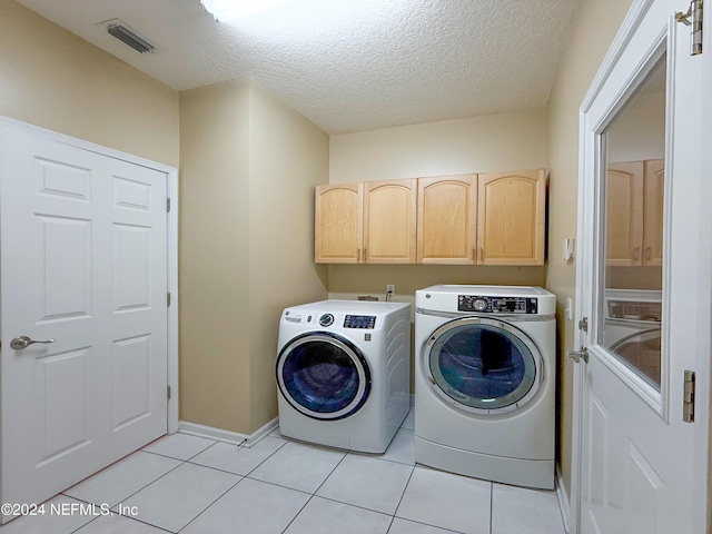 laundry area featuring washing machine and clothes dryer, light tile patterned floors, cabinets, and a textured ceiling