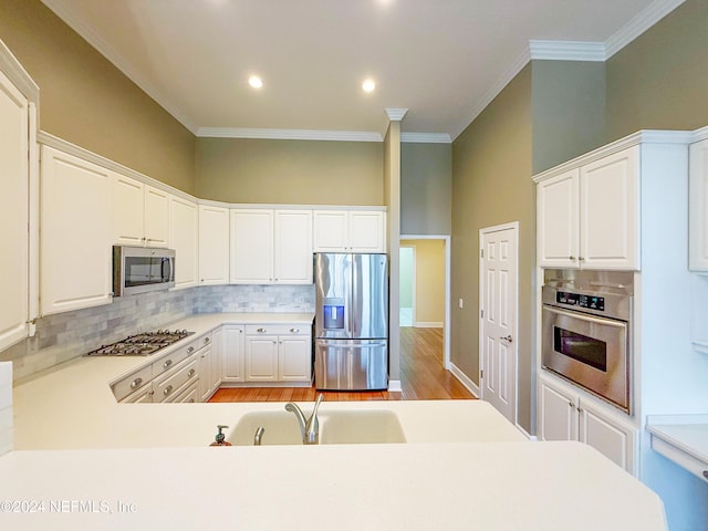 kitchen featuring backsplash, appliances with stainless steel finishes, crown molding, white cabinets, and light wood-type flooring