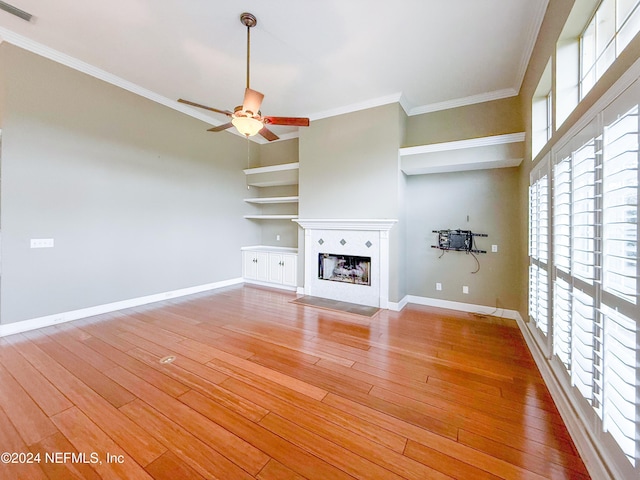 unfurnished living room featuring built in shelves, crown molding, hardwood / wood-style floors, and ceiling fan