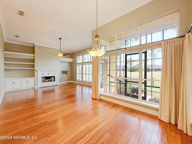 unfurnished living room featuring built in shelves, ceiling fan, wood-type flooring, and ornamental molding