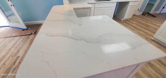 interior details with light stone countertops, light wood-type flooring, and white cabinetry