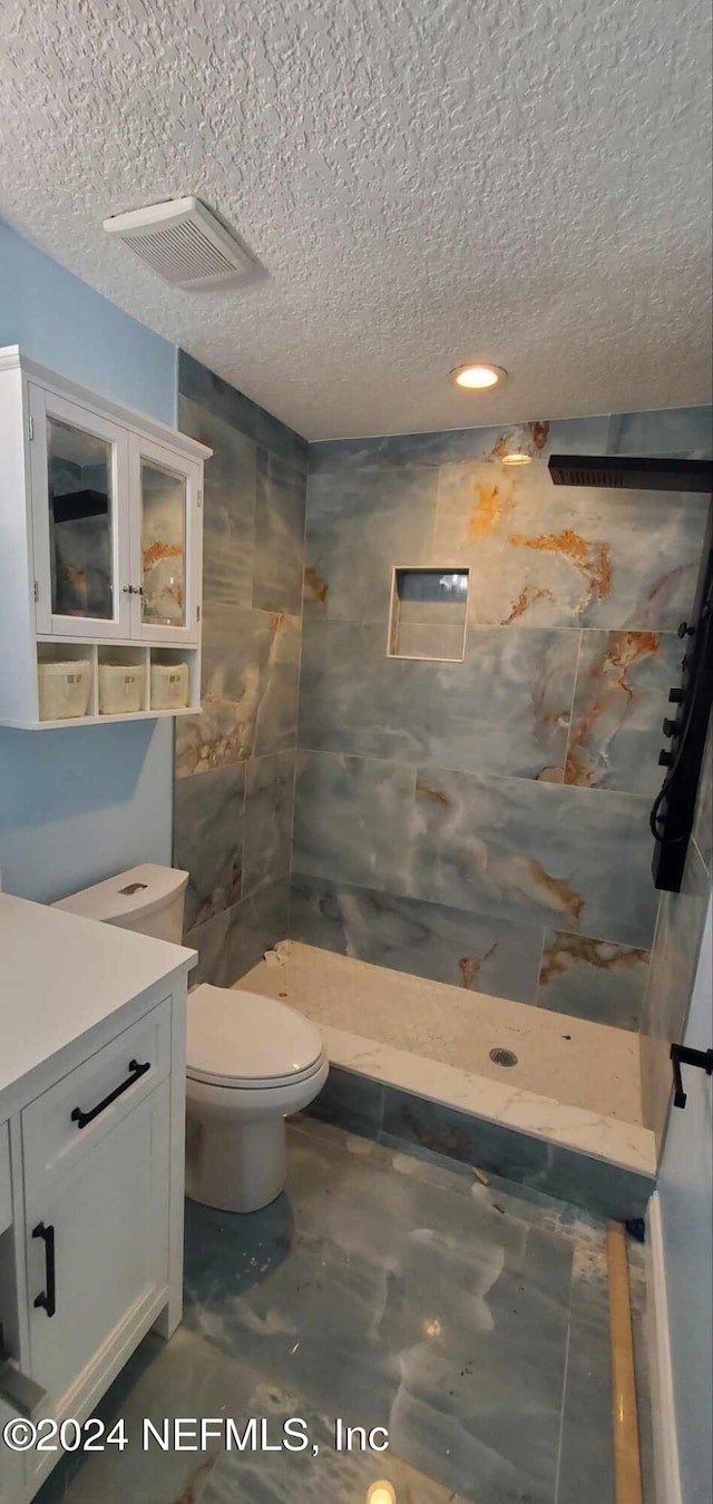 bathroom with tiled shower, vanity, a textured ceiling, and toilet