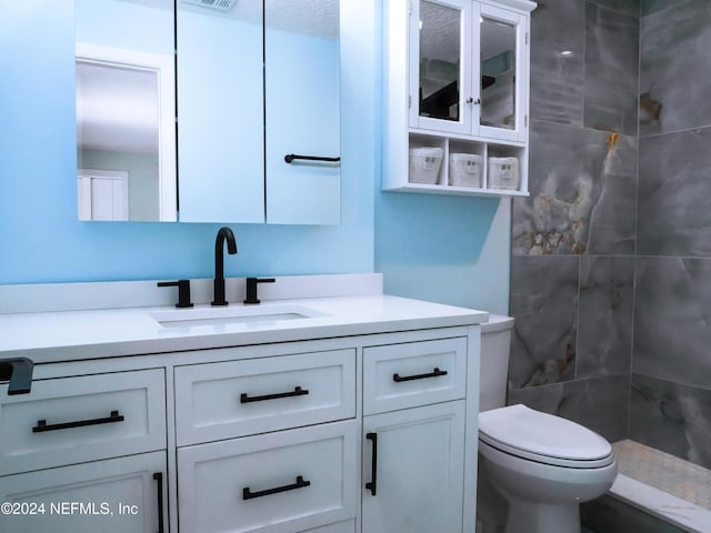 bathroom with a tile shower, vanity, a textured ceiling, and toilet