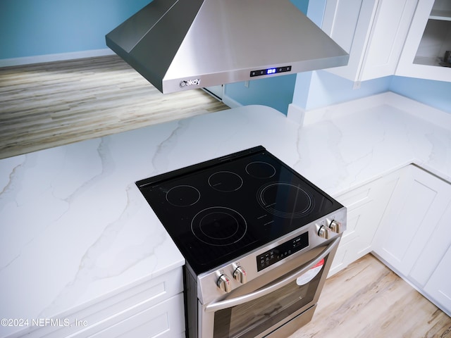 interior details with white cabinetry, light stone counters, extractor fan, stainless steel electric range, and light hardwood / wood-style floors