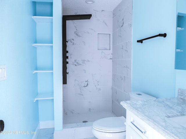 bathroom with a tile shower, vanity, and toilet