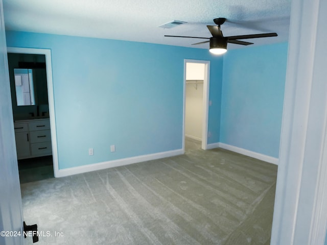 unfurnished bedroom featuring ensuite bath, ceiling fan, a walk in closet, light carpet, and a closet