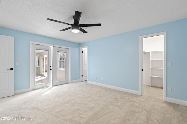 unfurnished bedroom with a textured ceiling, a spacious closet, access to outside, and light colored carpet