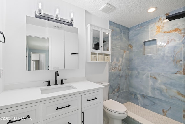 bathroom featuring vanity, a tile shower, toilet, and a textured ceiling