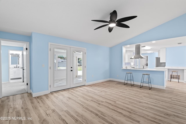 unfurnished living room with light wood-type flooring, french doors, ceiling fan, vaulted ceiling, and sink